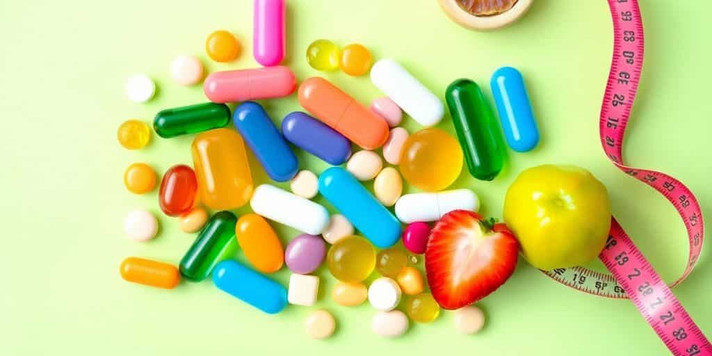 Colorful weight loss pills with fresh fruits and tape.