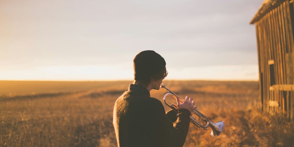 man playing trumpet outside house on field during daytime